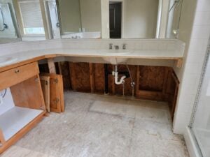 Bathroom sink with cabinet doors open and missing lower panels, exposing plumbing and wall framing beneath countertop.
