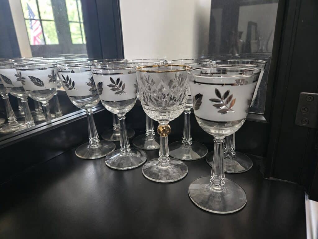 A group of clear wine glasses with silver leaf designs and one with a gold rim, emphasizing differentiation, are arranged on a black surface in front of a mirror.