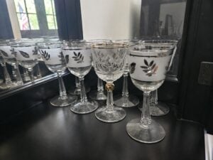 A group of clear wine glasses with silver leaf designs and one with a gold rim, emphasizing differentiation, are arranged on a black surface in front of a mirror.