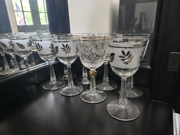 A group of clear wine glasses with silver leaf designs and one with a gold rim, emphasizing differentiation, are arranged on a black surface in front of a mirror.